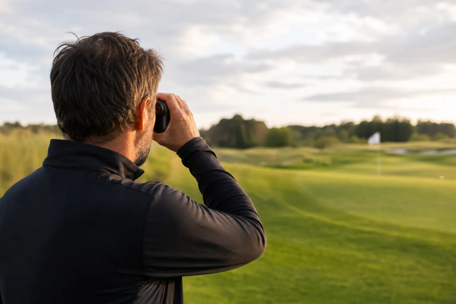 Golfare håller upp en laseravståndsmätare och siktar mot flaggan på en green