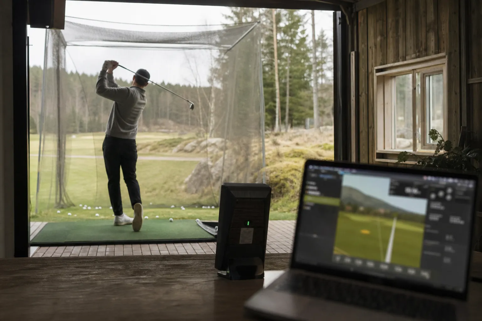 Launch monitor placerad bakom en golfare som slår bollar mot ett nät inomhus